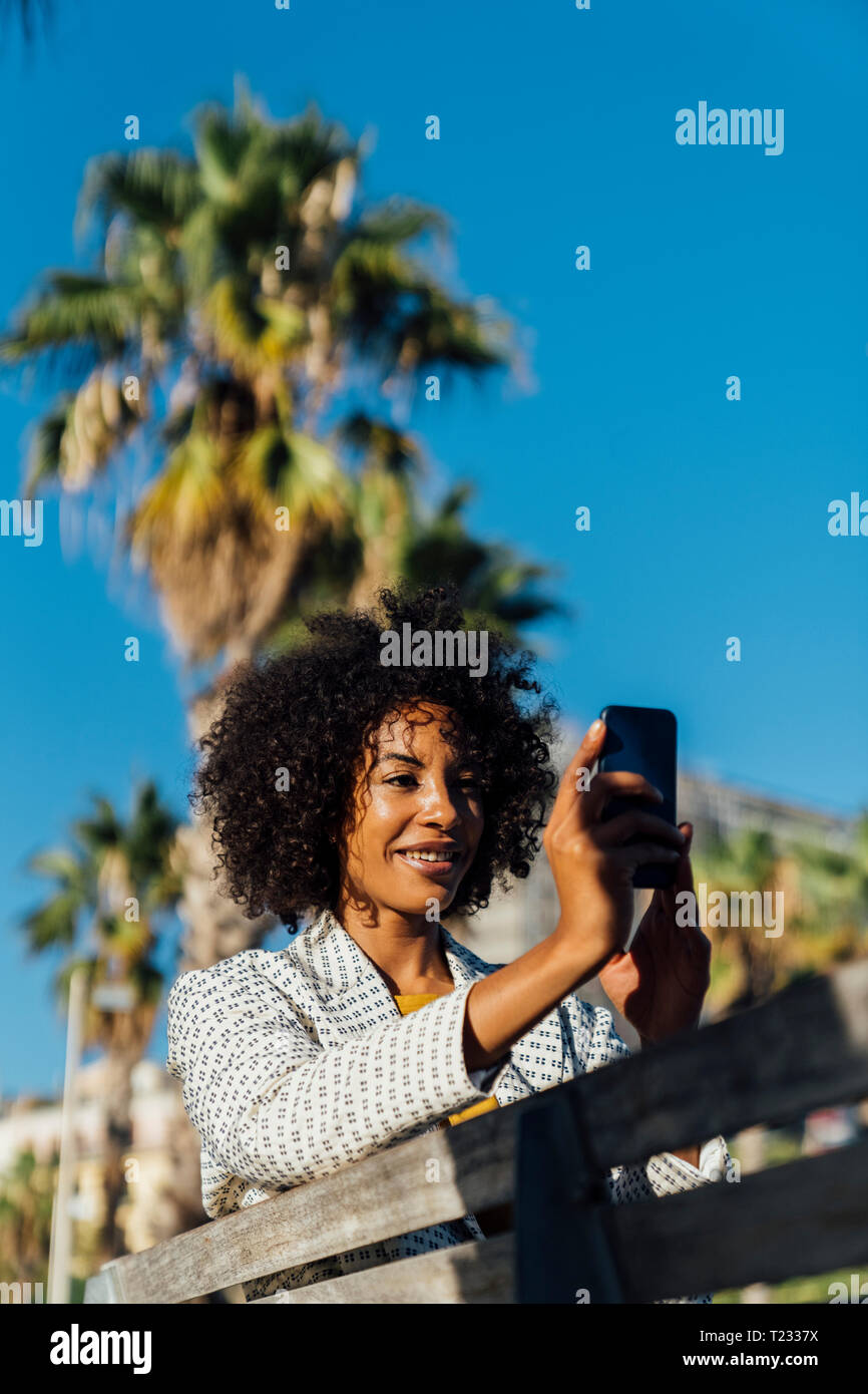 Belle femme assise sur un banc dans la ville, takig photos avec son smartphone Banque D'Images