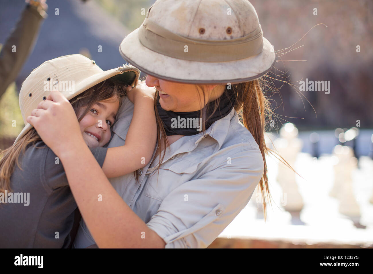 Happy girl embracing woman wearing pith helmet Banque D'Images