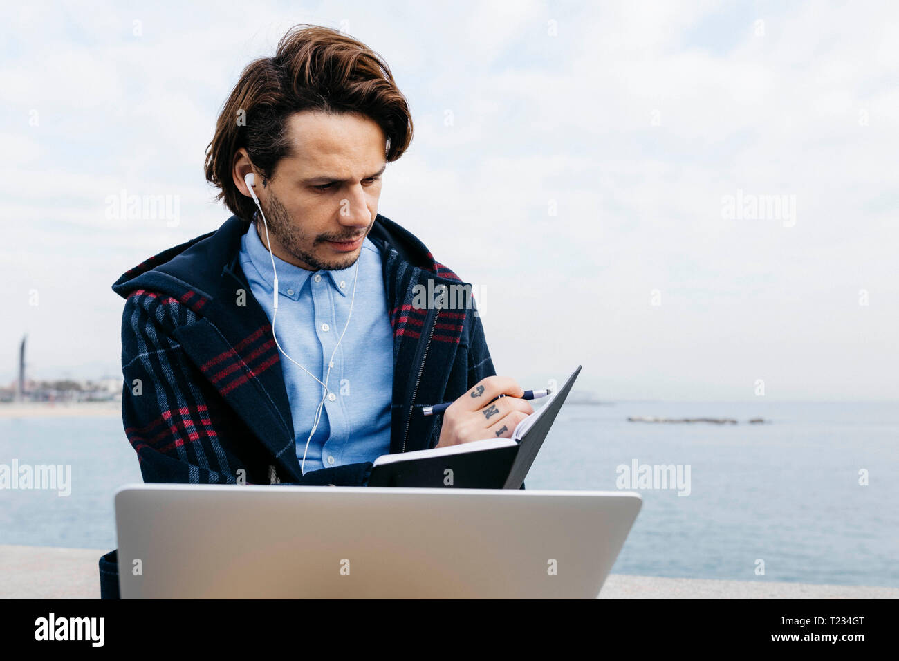 Espagne, Barcelone, l'homme assis à la mer le travail avec ordinateur portable et ordinateur portable Banque D'Images