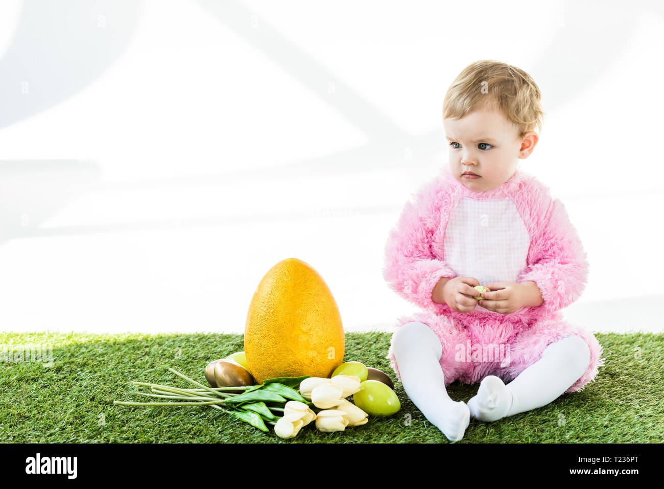 Adorable enfant en costume rose fluffy assis près de l'œuf d'autruche jaune coloré, les oeufs de poule et tulipes isolated on white Banque D'Images