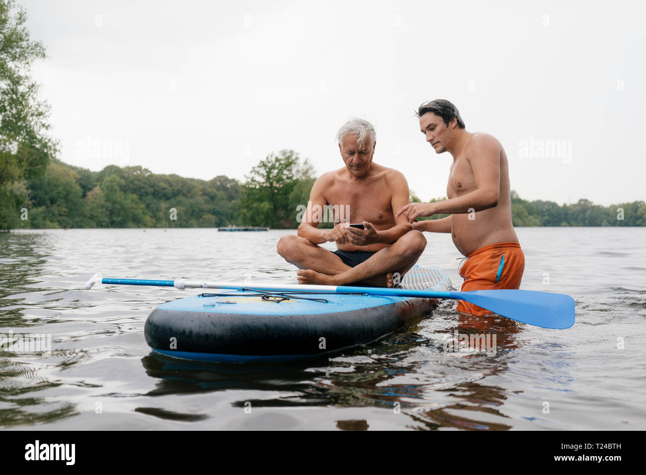 Les personnes âgées et les jeunes avec l'homme du Conseil SUP sur un lac using cell phone Banque D'Images