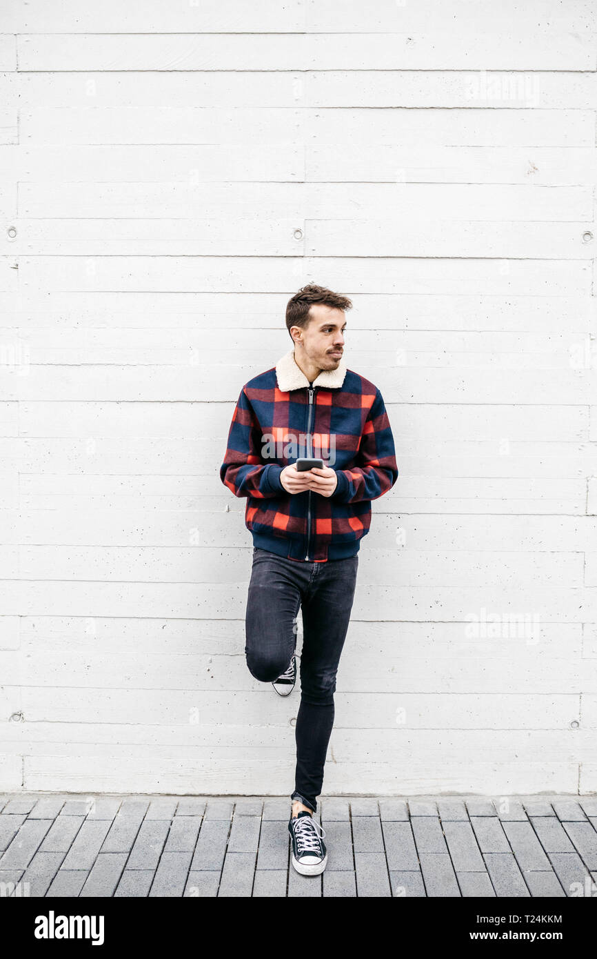 Jeune homme à la veste rouge et bleu à l'aide d'un téléphone dans un mur blanc Banque D'Images