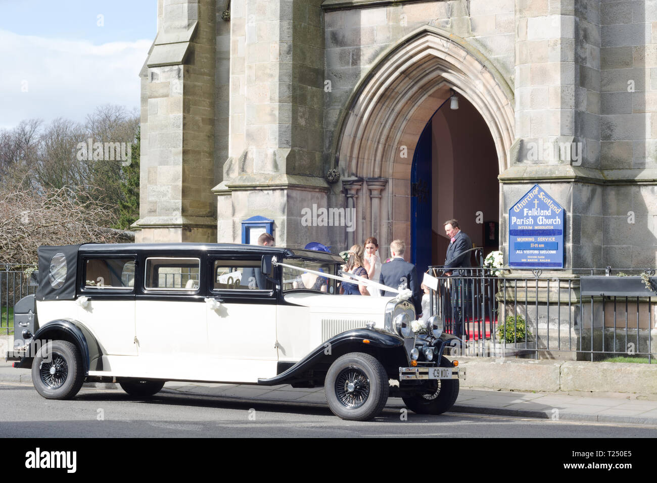 Un mariage vintage voiture garée à l'extérieur de l'église, de Falkland, en Écosse. Mariée de demoiselle d'honneur, cérémonie à la porte avant Banque D'Images