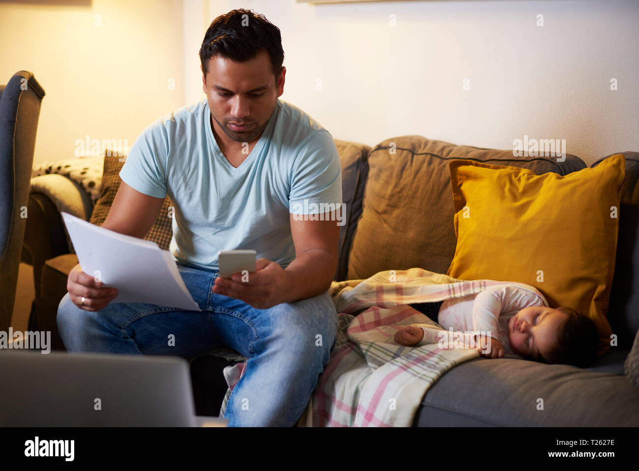 Le multitâche père travaillant à la maison avec bébé girl sleeping on sofa Banque D'Images