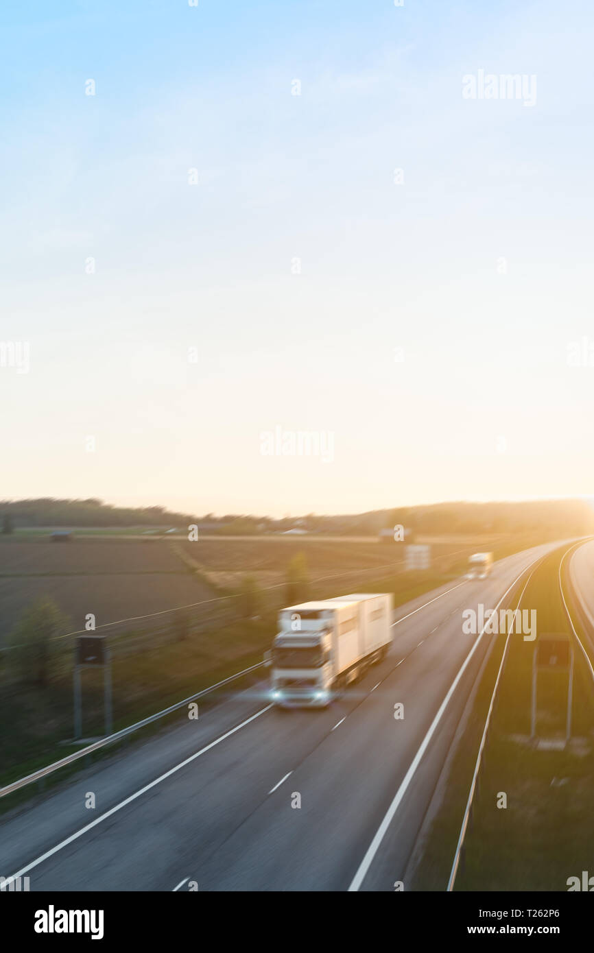 Deux camions de fret roulant sur l'autoroute au coucher du soleil avec effet de flou. Banque D'Images