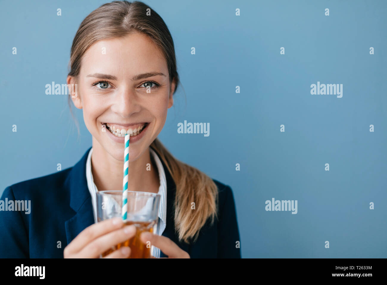 Portrait of a young woman contre fond bleu, boire du thé glacé avec une paille Banque D'Images