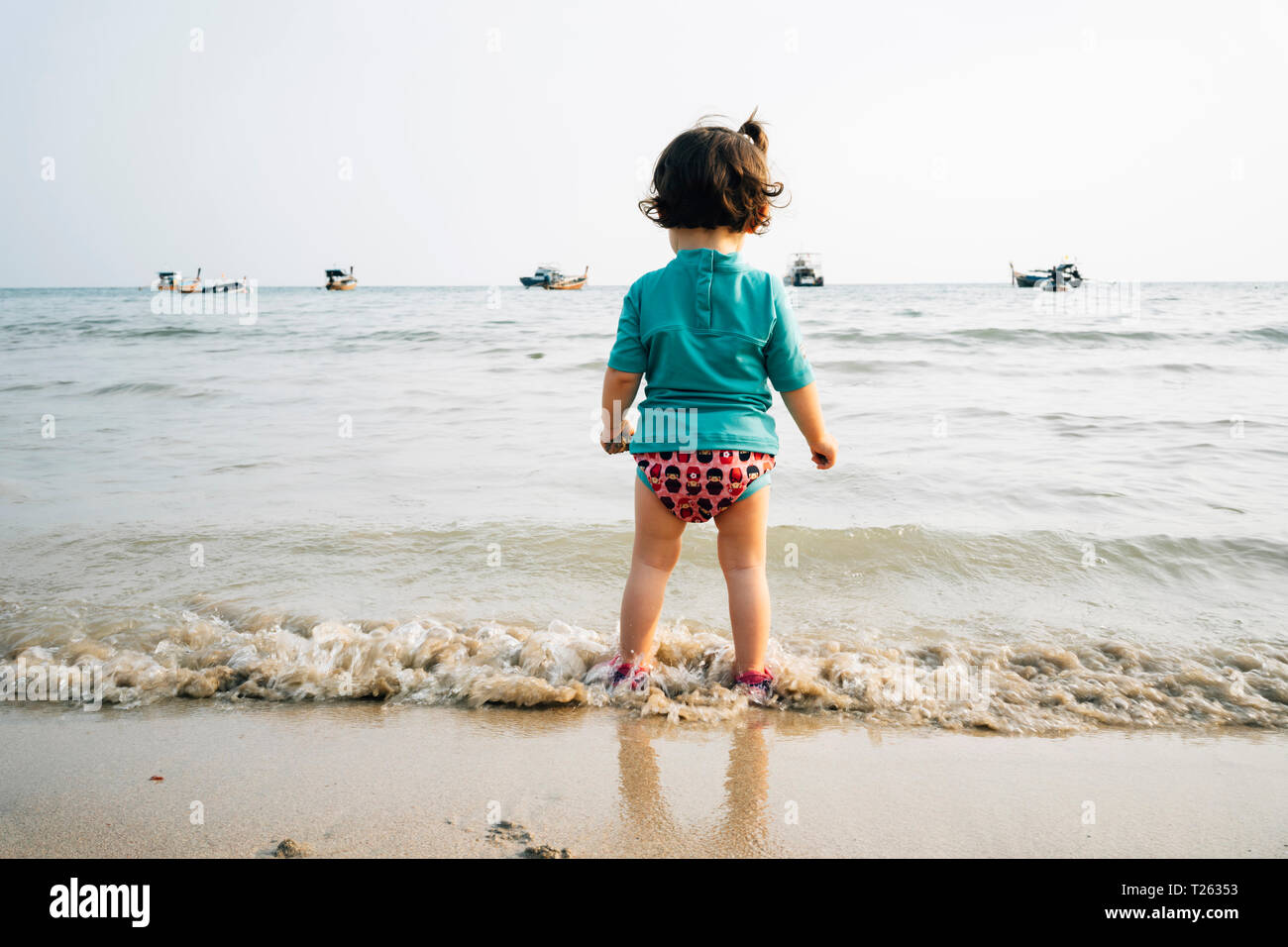 La Thaïlande, Koh Lanta, vue arrière de baby girl wearing UV protection shirt standing at seashore Banque D'Images