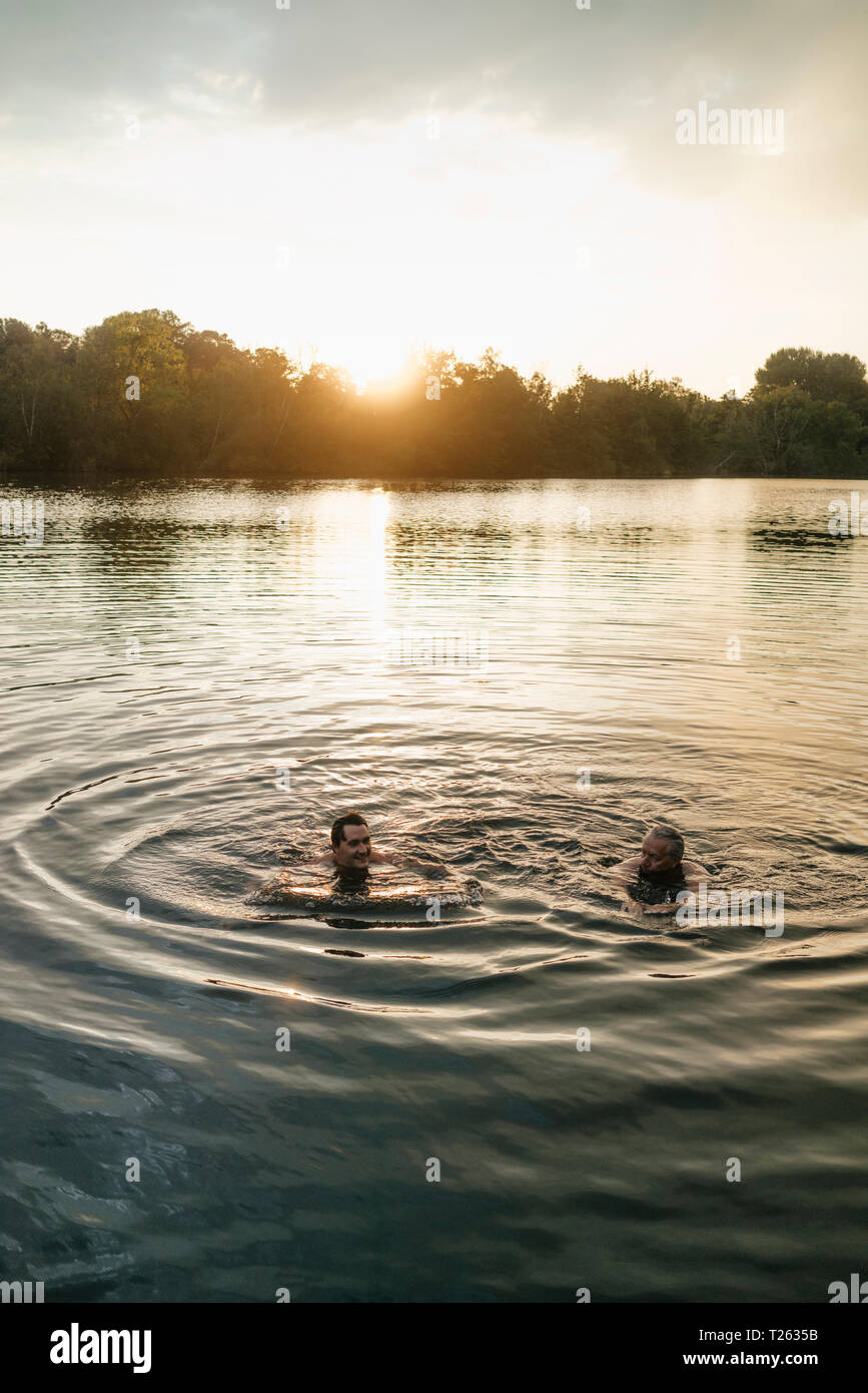 Vieux et jeune homme nageant dans un lac au coucher du soleil Banque D'Images