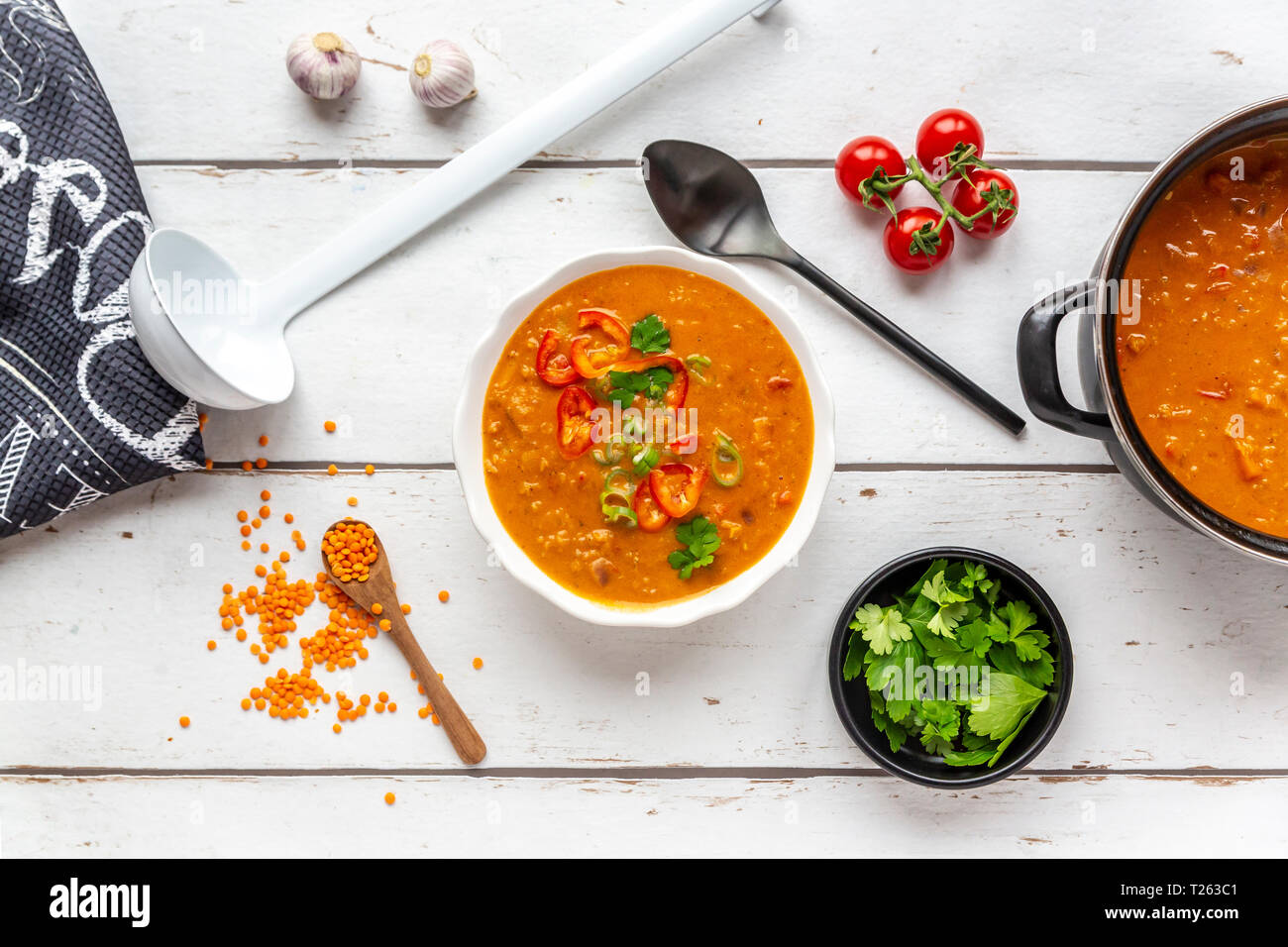 Bol et pot de soupe aux lentilles rouges garnie et ingrédients sur bois blanc Banque D'Images