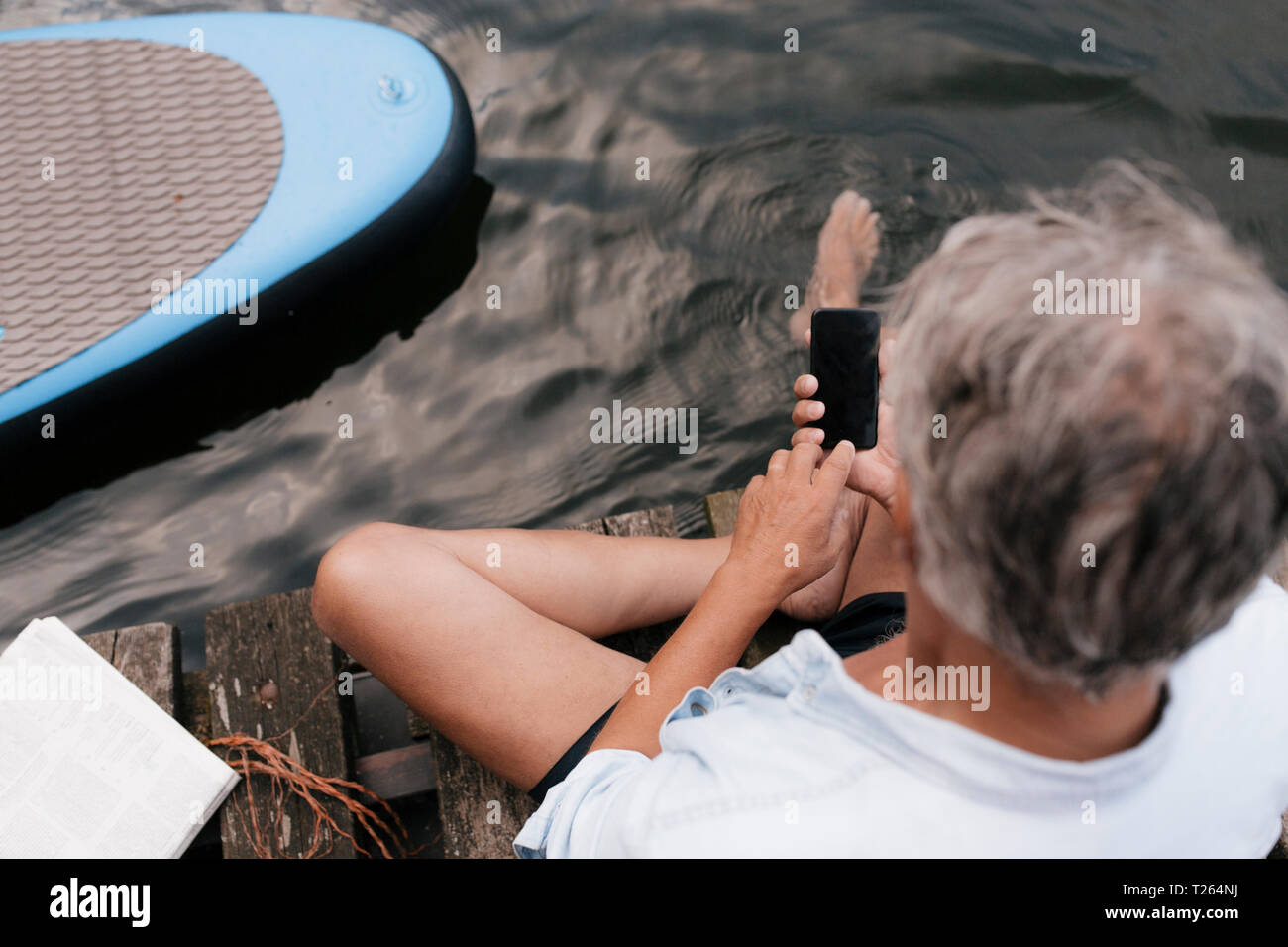 Senior man sitting on jetty à un lac à l'aide de téléphone cellulaire Banque D'Images