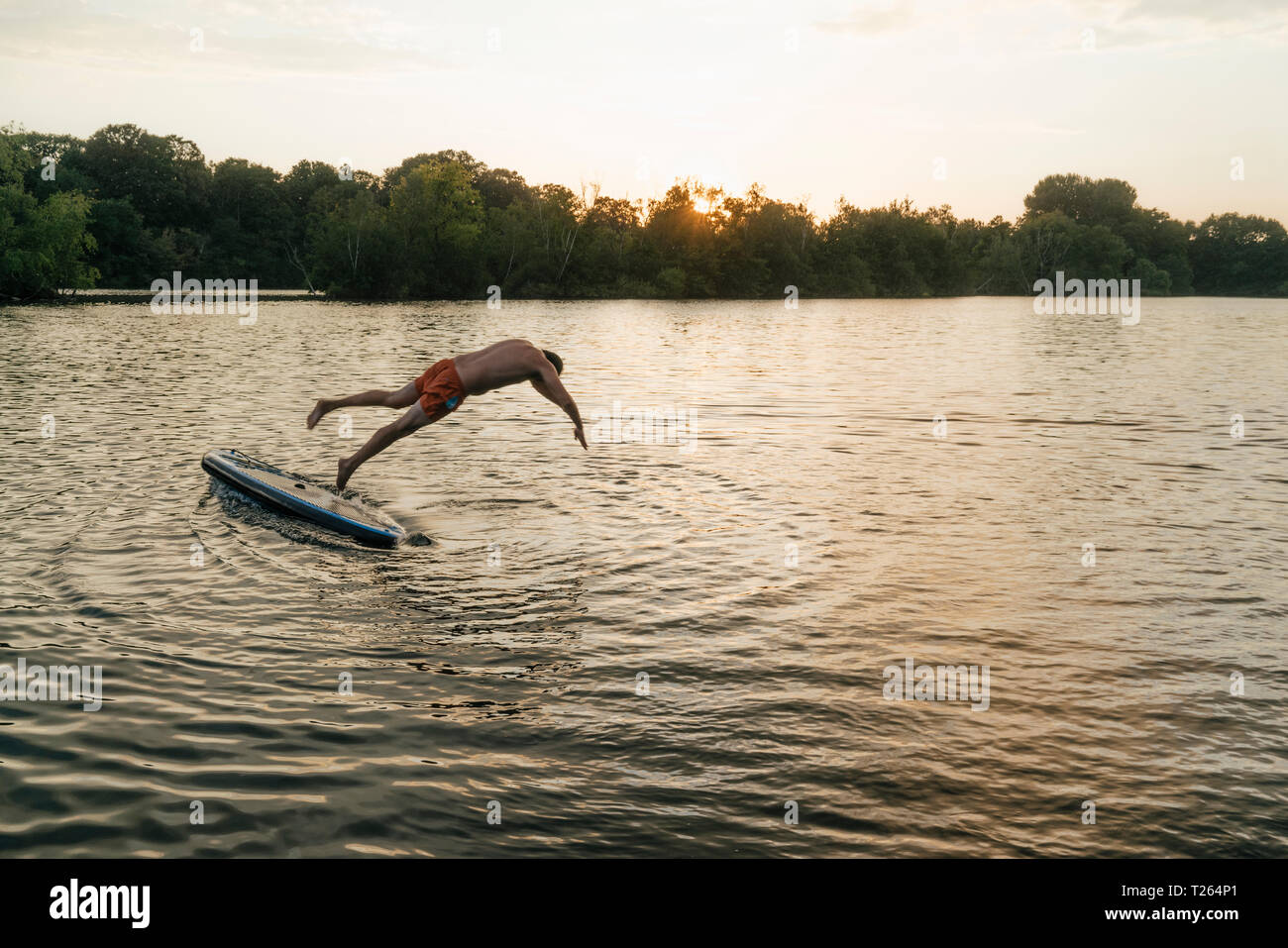 Man jumping de SUP sur un lac au coucher du soleil Banque D'Images