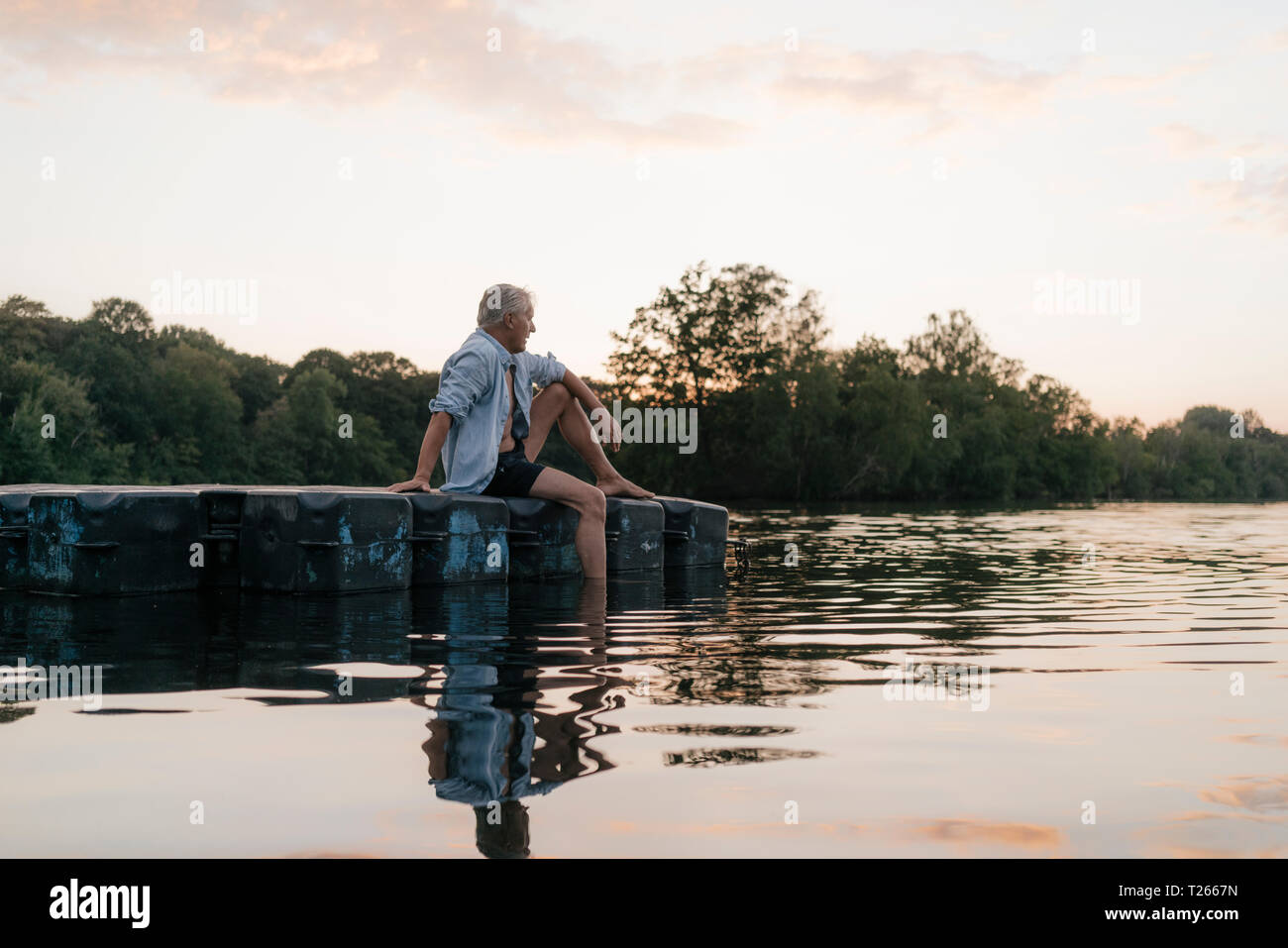 Senior man sitting on raft dans un lac au coucher du soleil Banque D'Images