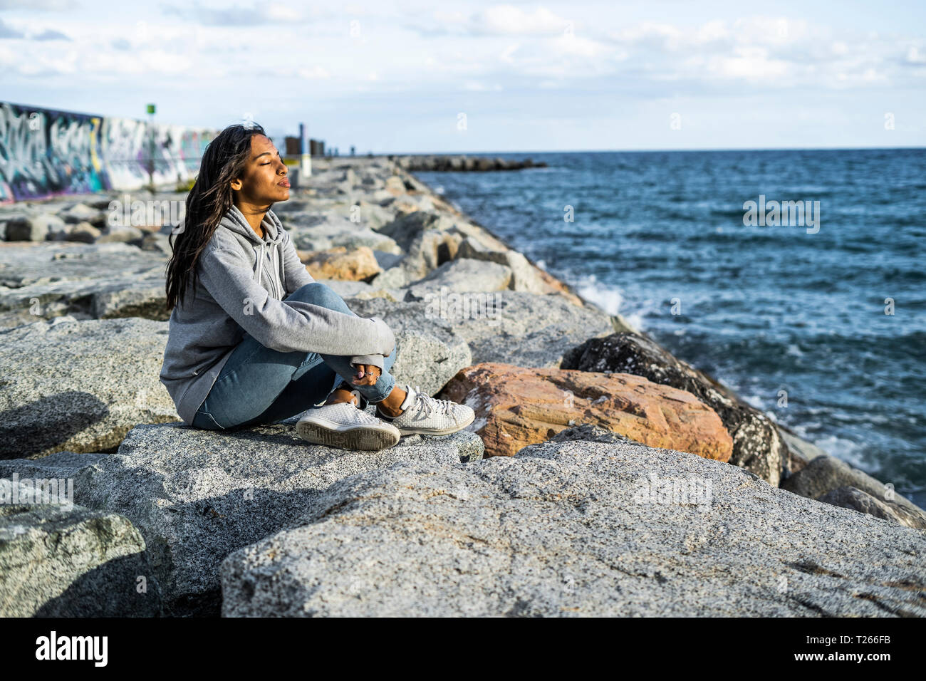 Jeune femme de détente sur la plage, assis sur des rochers, les yeux fermés Banque D'Images