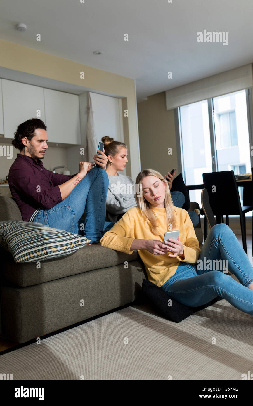 Ennuyer friends sitting on couch in living, à l'aide d'appareils numériques Banque D'Images