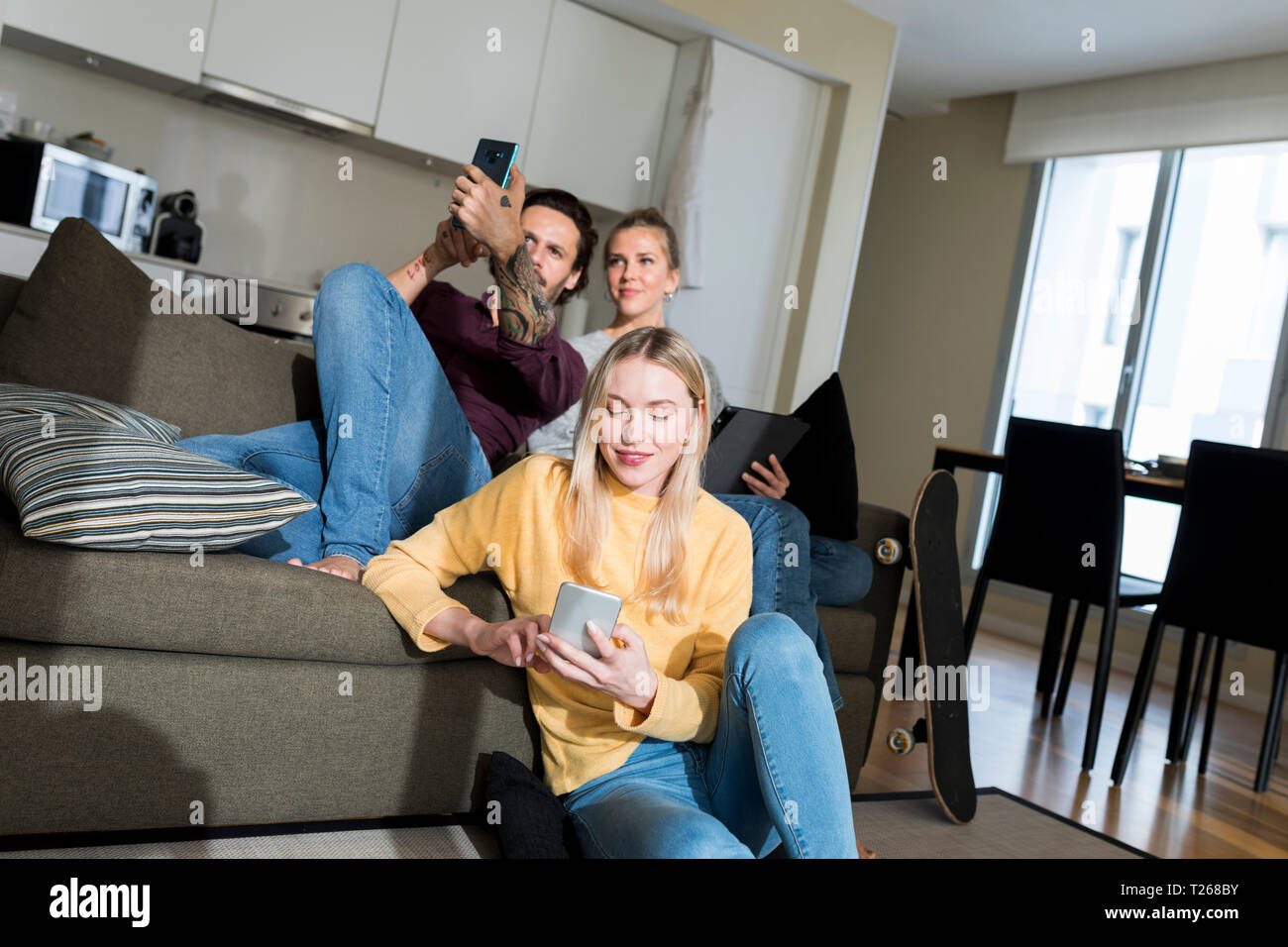 Friends sitting on couch in living, à l'aide d'appareils numériques Banque D'Images