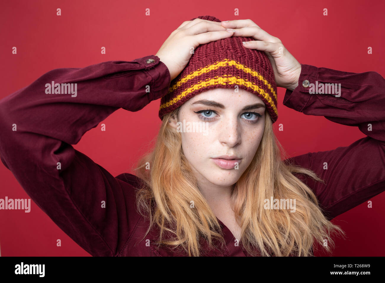 Portrait of young woman wearing hat laineux en face de fond rouge Banque D'Images