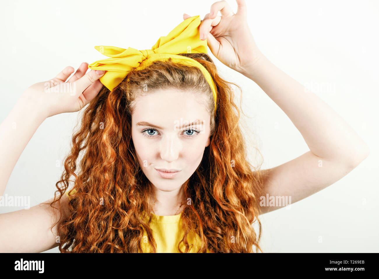 Portrait de curly redhead girl wearing yellow t-shirt bow jaune se redresse sur sa tête en étant debout sur le fond blanc Banque D'Images