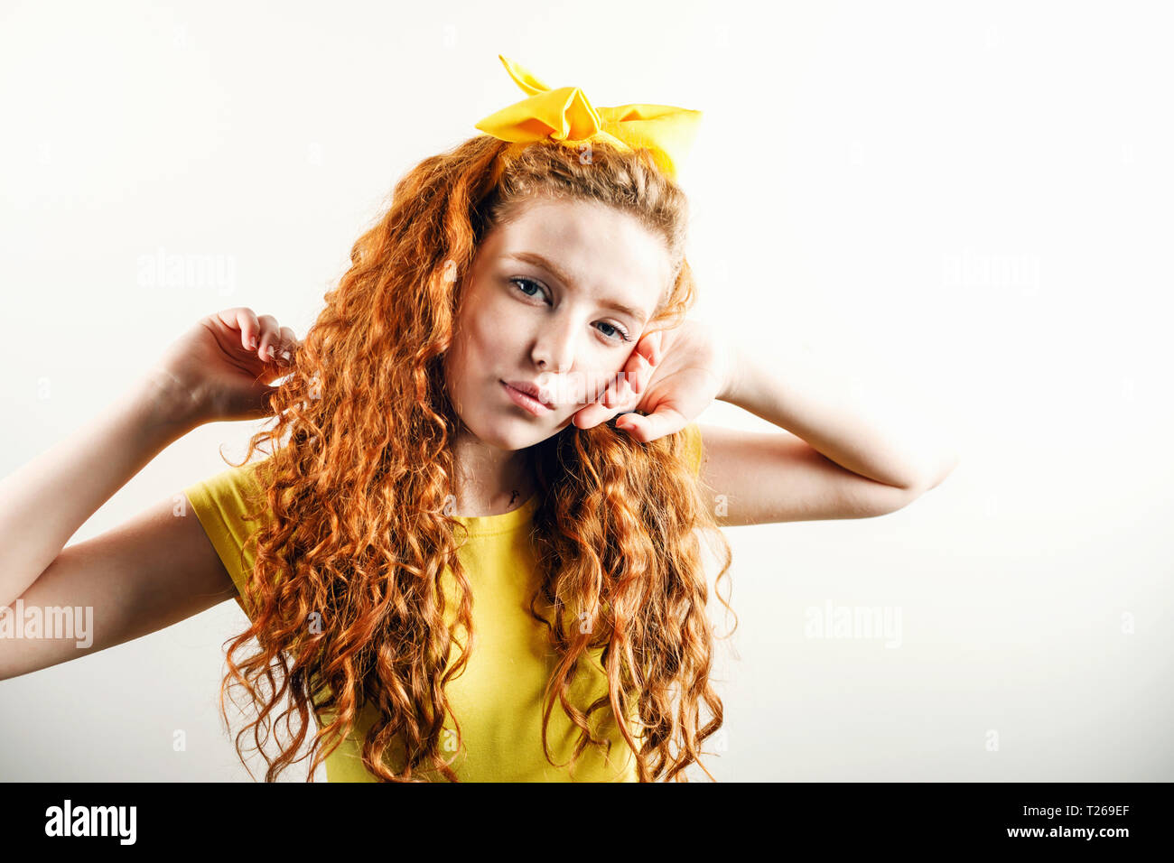 Portrait de jeune fille rousse bouclée avec un arc jaune sur sa tête portant des T-shirt jaune posant sur le fond blanc Banque D'Images