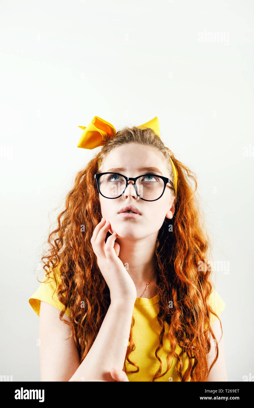 Jeune fille rousse frisée pensif en spectacles avec un arc jaune sur sa tête portant des T-shirt jaune jusqu'à la pensée et Banque D'Images