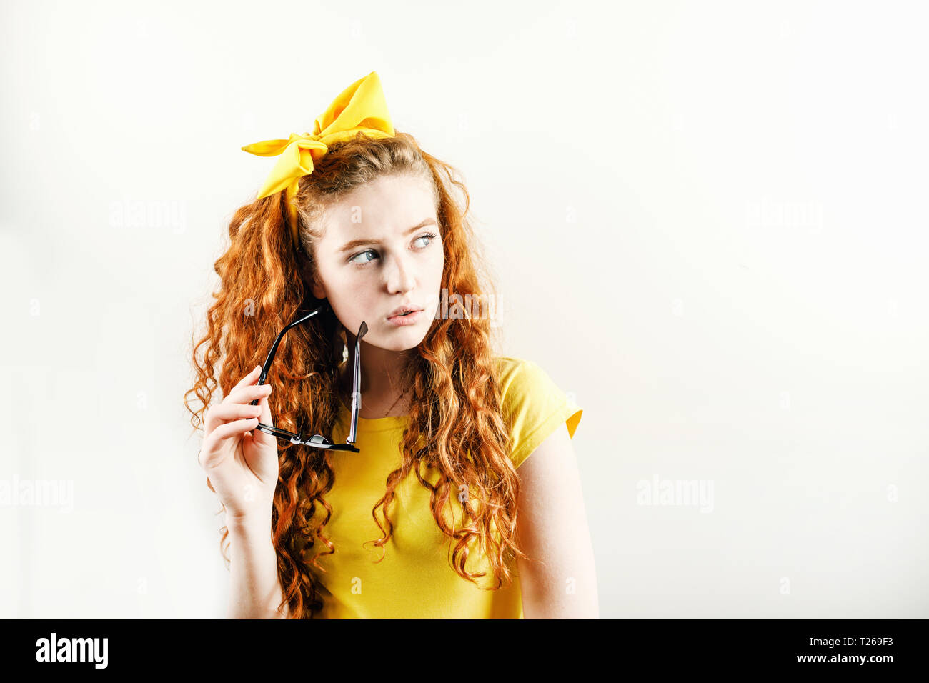 Pensive curly redhead girl avec un arc jaune sur sa tête portant des T-shirt jaune et à la suite des spectacles holding Banque D'Images
