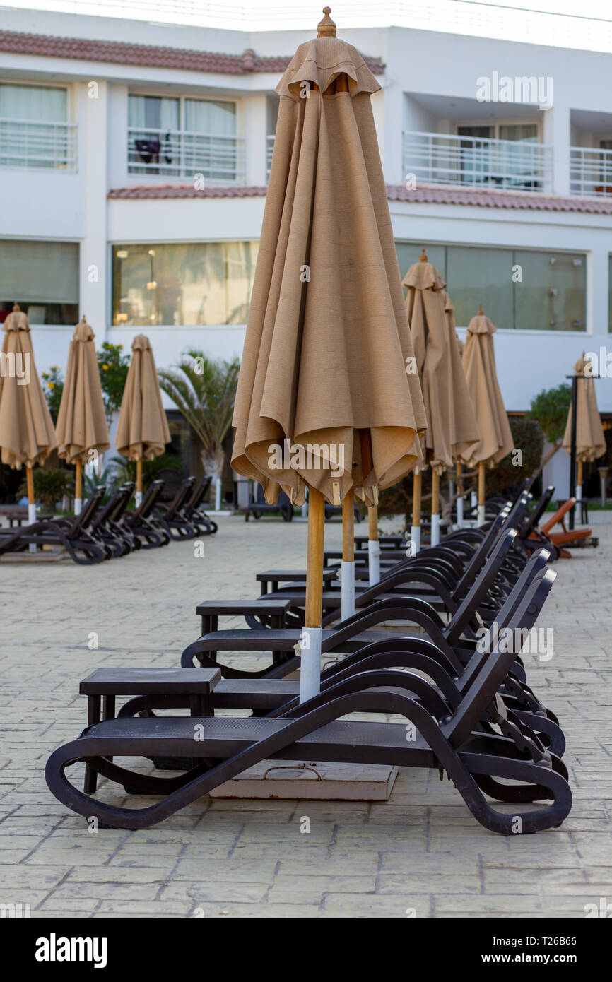Plusieurs rangées de chaises longues de plage vide près de la piscine de l'hôtel fermée sous des parasols. Beach lounges, laissant en perspective. Des chaises longues en vide Banque D'Images