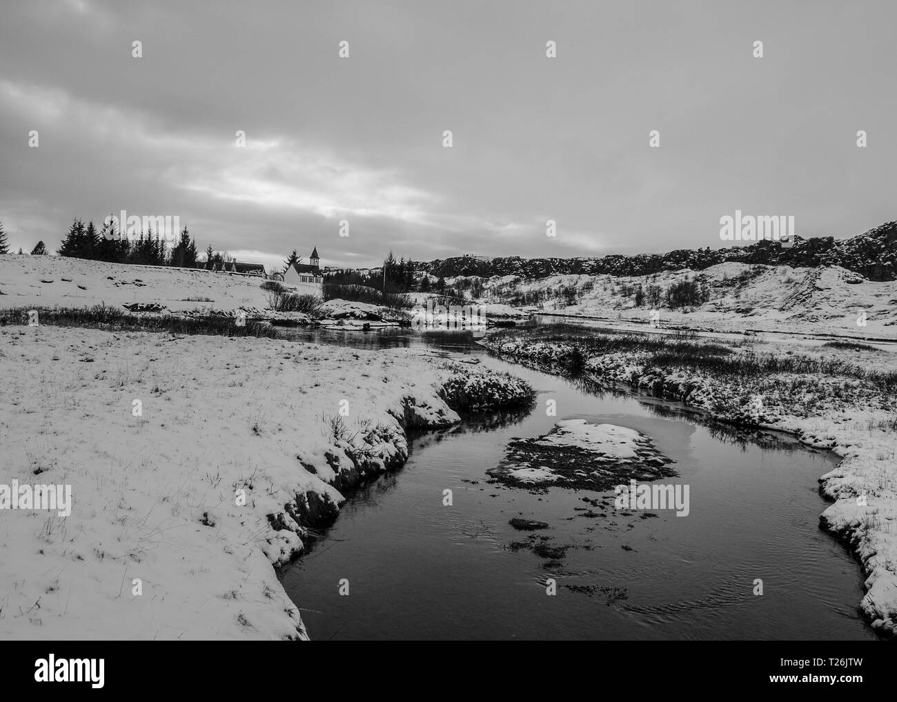 Une rivière traverse la neige dans un noir et blanc tourné d'un paysage islandais. Banque D'Images