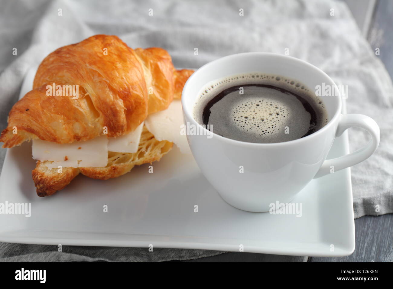 Petit-déjeuner français : croissant sandwich avec du fromage et une tasse de café noir Banque D'Images