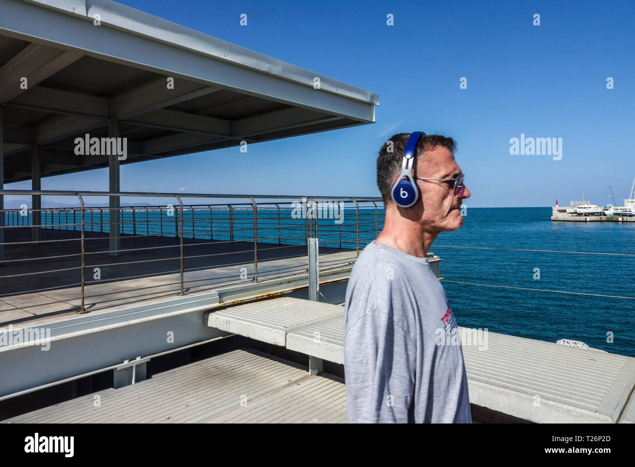 Écouteurs homme senior sur la jetée en béton mer à l'arrière Valencia Port Espagne adulte senior 50s écouter de la musique écouteurs de musique adulte senior Banque D'Images