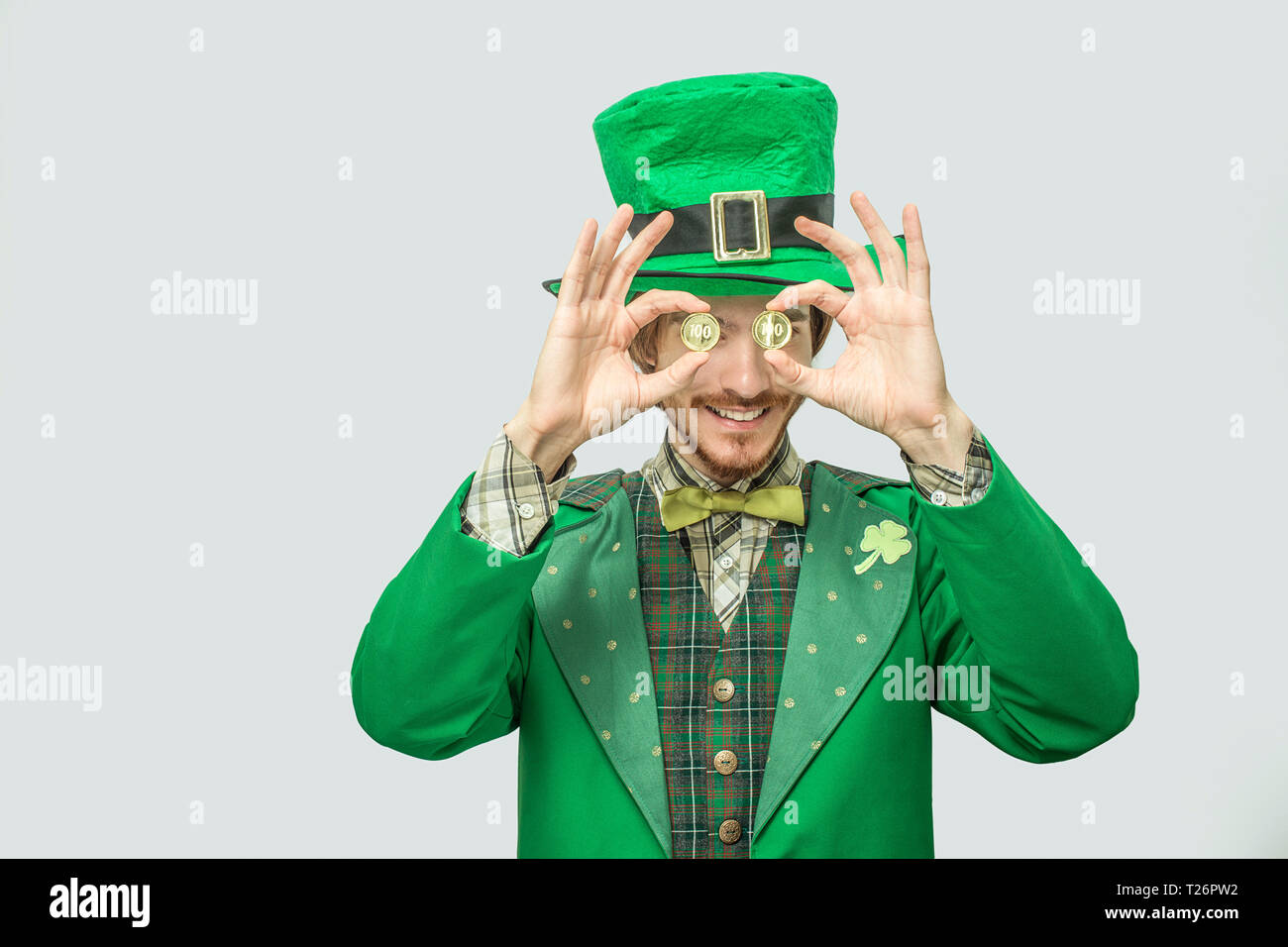 Heureux jeune homme riche en costume vert tenir deux pièces d'or devant les yeux. Il sourire et l'air heureux. Guy, portent des costumes du saint Patrick. O isolés Banque D'Images