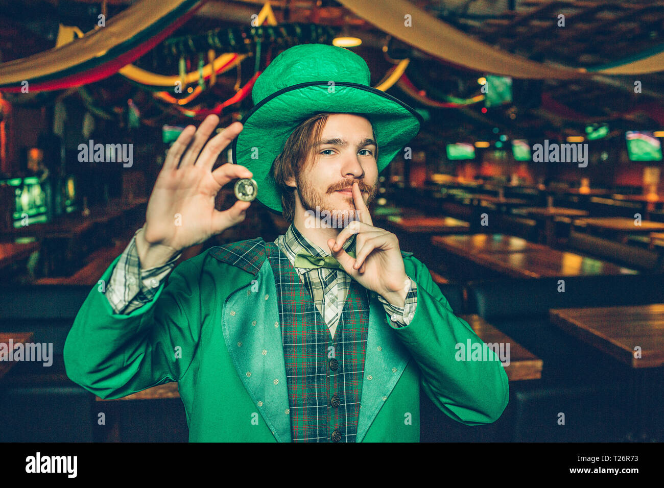 Heureux jeune homme riche dans la Saint-Patrick, la fonction de la parole à pub et pièce d'or en attente. Il a doigt près de la bouche. Guy rechercher sur appareil photo. Il stand alone Banque D'Images