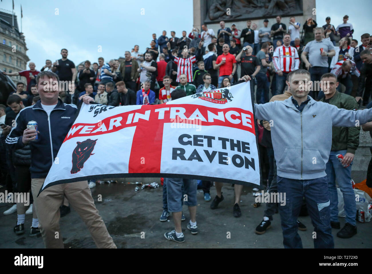 Londres, Royaume-Uni. 30 mars 2019. Une foule nombreuse de fans de football de Sunderland A.F.C. dans un Trafalgar Square, arborant un drapeau anglais modifié avec le logo du club et des slogans EN TRANSE et METTANT LE FEU À LA RAVE. La scène capture l'énergie et l'identité de la culture du football nord-anglais. Les supporters itinérants de Sunderland dans la soirée précédant leur finale EFL Trophy contre Portsmouth à Wembley prennent Trafalgar Square. Penelope Barritt/Alamy Live News Banque D'Images
