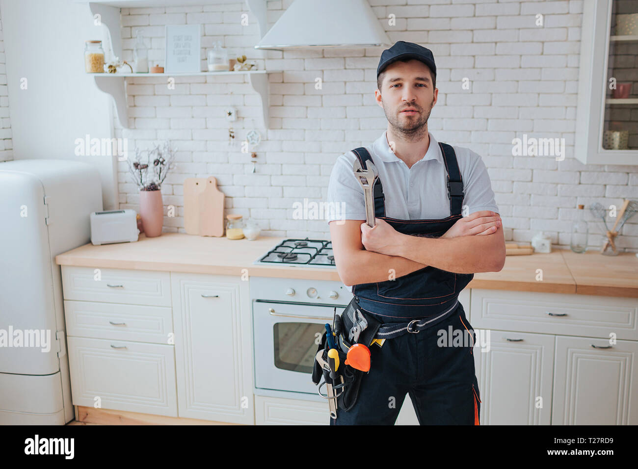 Plombier en cuisine. Un regard professionnel sur la caméra et la pose.  Mains croisées. Outils sur côté de la courroie Photo Stock - Alamy