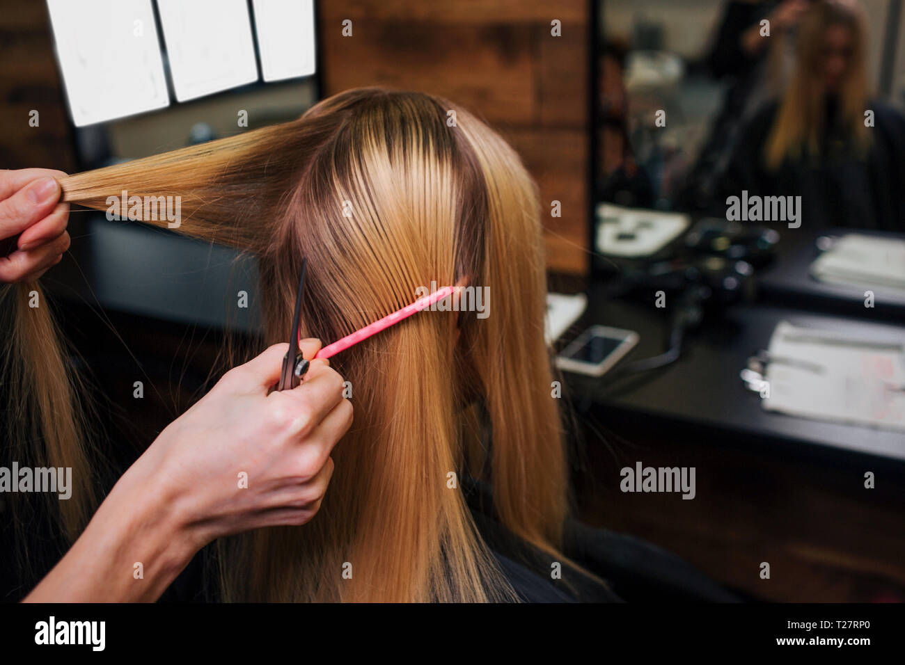 Hairstylist hands holding strand de cheveux blonds tandis qu'il coupe les cheveux mouillés avant de salon Banque D'Images
