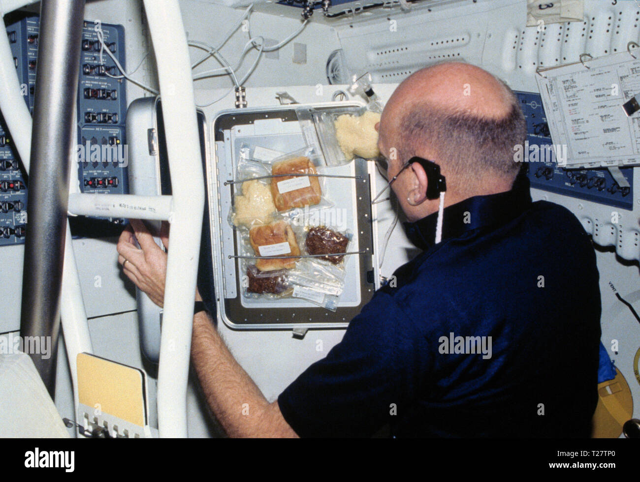 (Mars 1982) --- L'astronaute C. Gordon Fullerton, STS-3, le pilote utilise les deux mains pour récupérer une partie du repas à partir d'un test en vol orbital plus chaud des aliments dans le compartiment intermédiaire de la navette spatiale en orbite autour de la Terre Colombie-Britannique. Banque D'Images