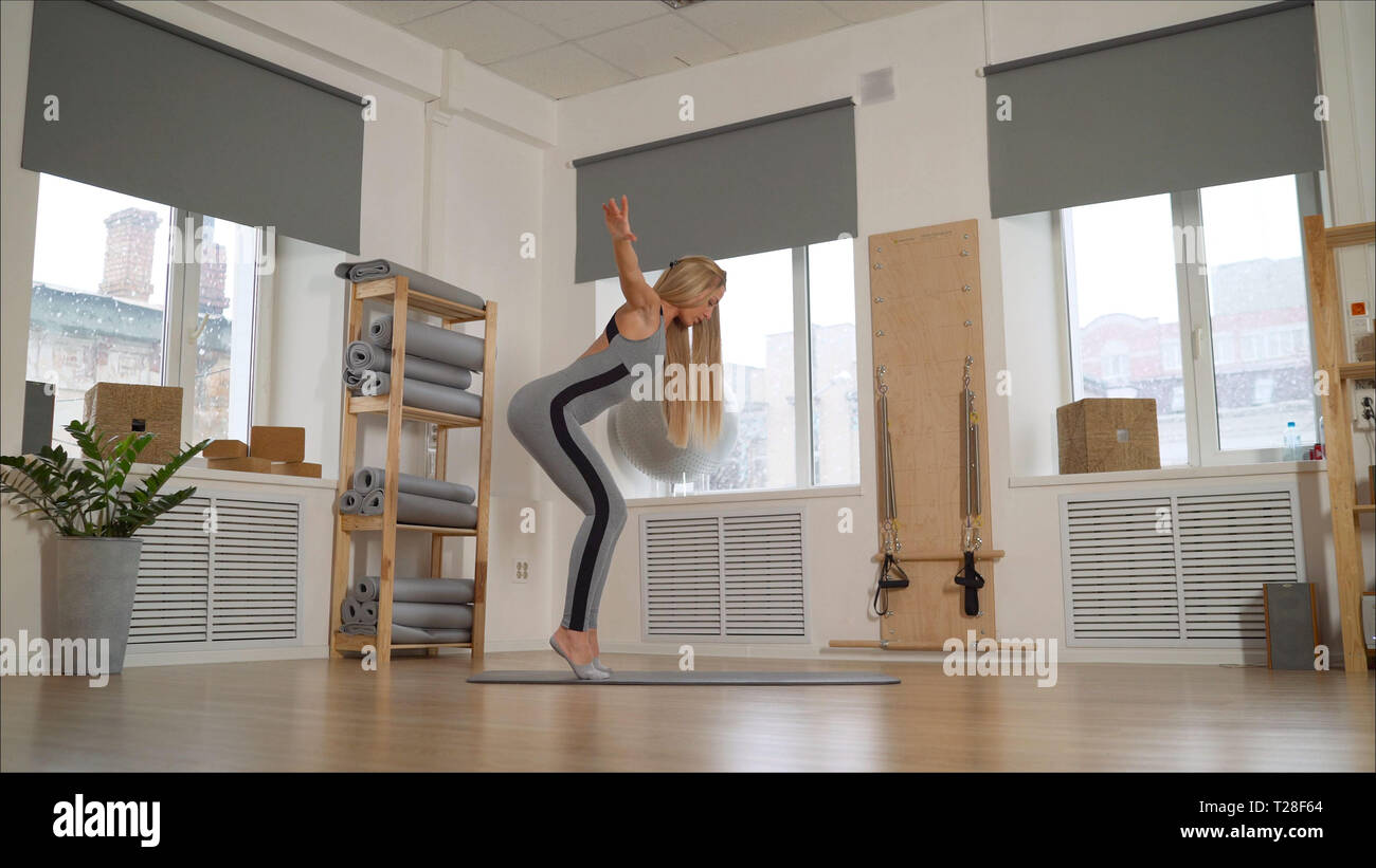 Athletic jeune fille brune dans un costume gris s'est engagé dans l'étirement. Fille Slim engagées professionnellement dans Pilates. Banque D'Images