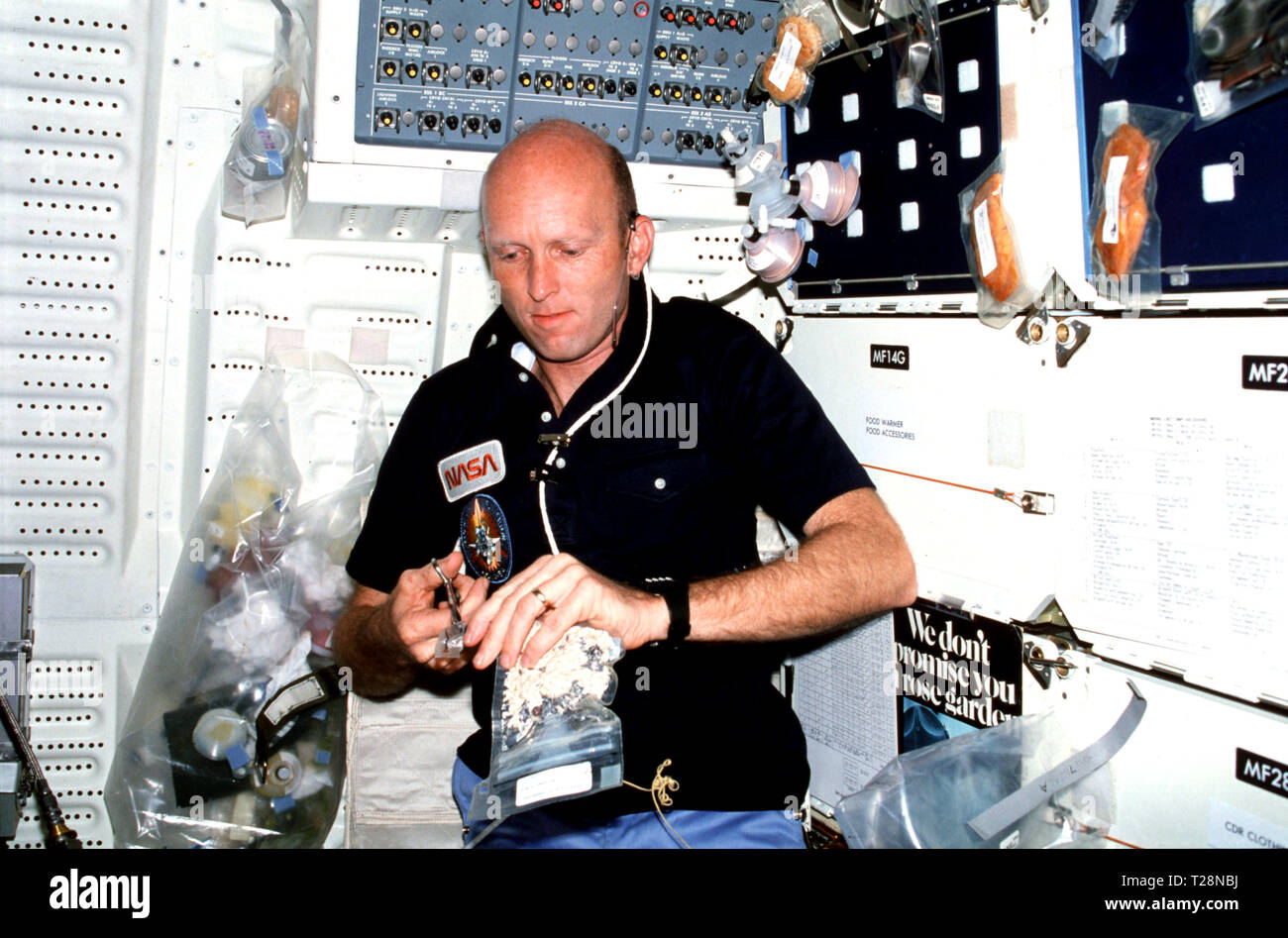 M003-26-253 (30 mars 1982) --- Pilote C. Gordon Fullerton, le port de kit de communication (assy) casque (mini-HDST), prépare des repas sur compartiment intermédiaire. Clips de Fullerton (céréales alimentaires déshydratées) forfait avec des ciseaux. L'ouverture permettra à Fullerton pour insérer JSC kit canon à eau distributeur d'eau pour chauffer matières avec de l'eau chaude. Plateau à repas ensemble est fixé à l'avant compartiment intermédiaire locker et détient plus d'emballages d'aliments et les contenants de boisson. Banque D'Images