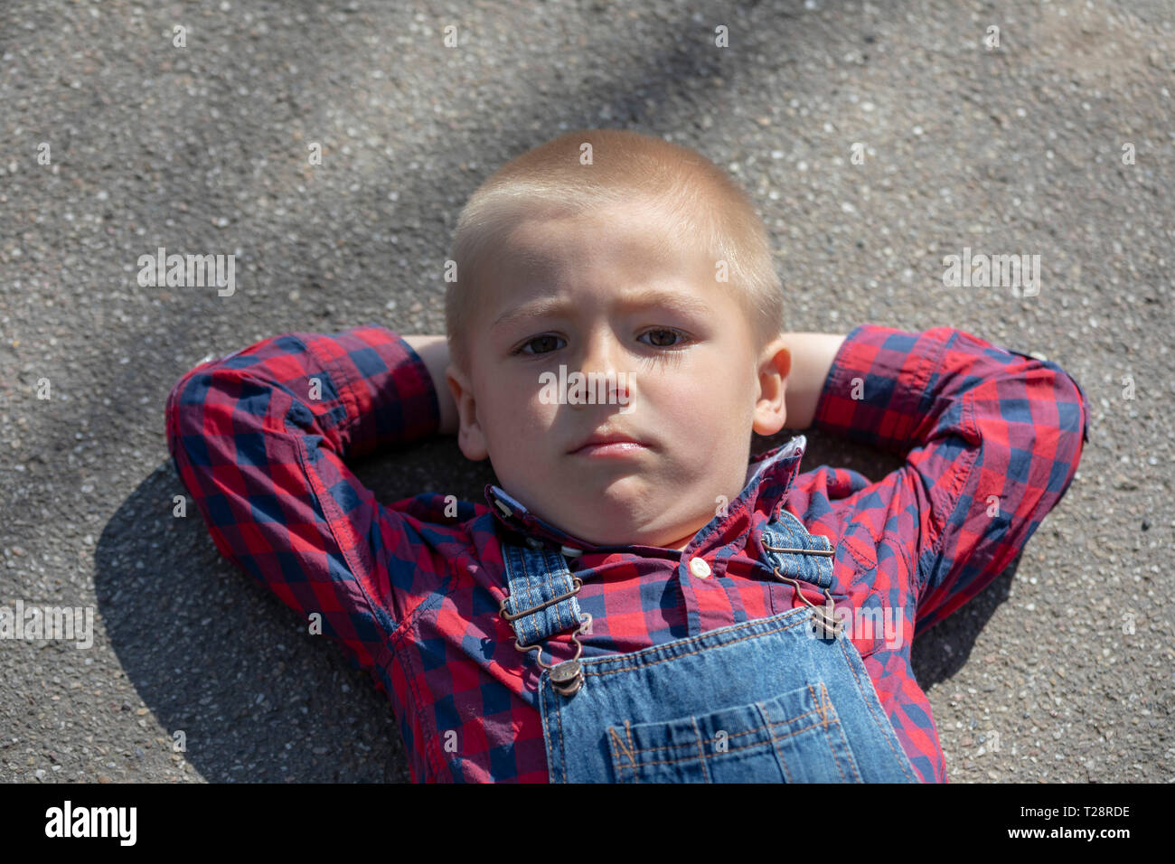 Enfant se trouvant sur le plancher à l'arrière, à la longue. Garçon réfléchi portrait couché sur bras croisés regarder dans la distance Banque D'Images