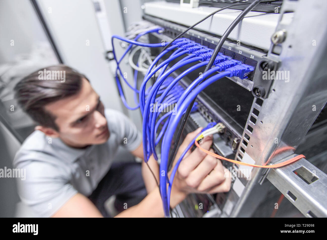 Jeune homme travaillant dans la salle des serveurs du réseau de fibre optique avec noeud pour les communications numériques et internet Banque D'Images