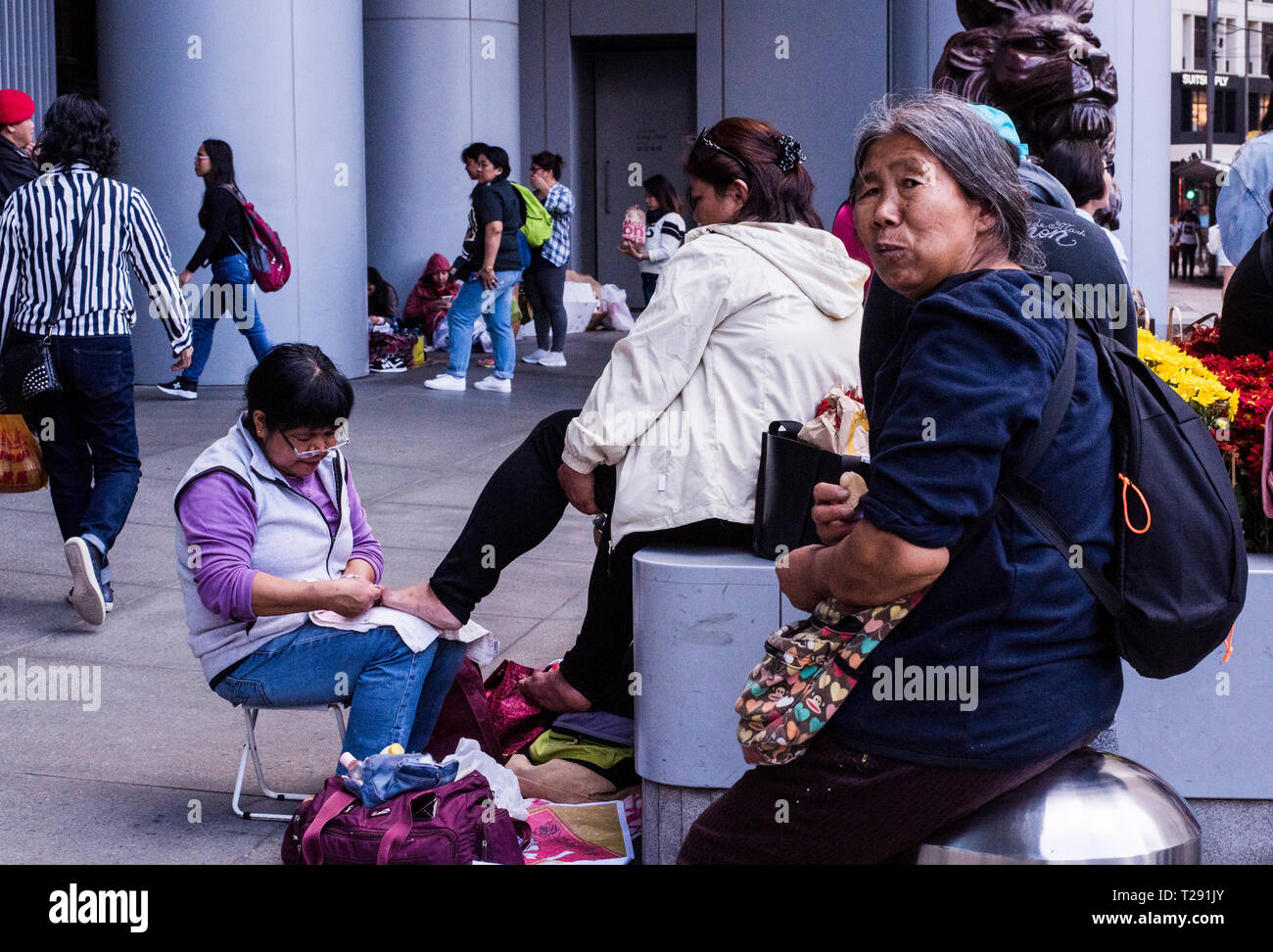 Femme pédicure dans rue passante, femme plus âgée en premier plan, Kowloon, Hong Kong Banque D'Images