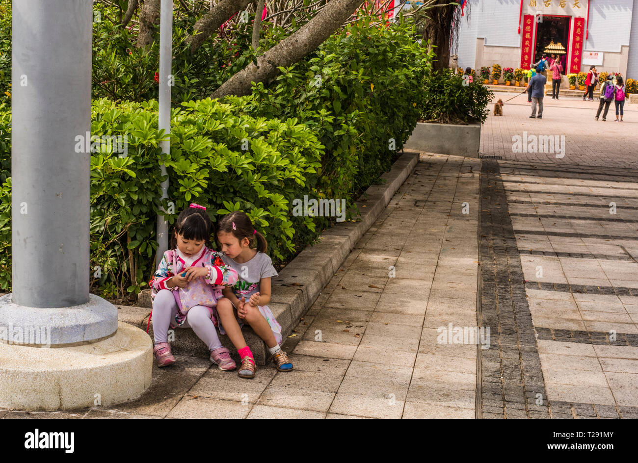 Deux jeunes filles, assis sur le coin du mur, dans le village balnéaire de Stanley, Hong Kong Banque D'Images