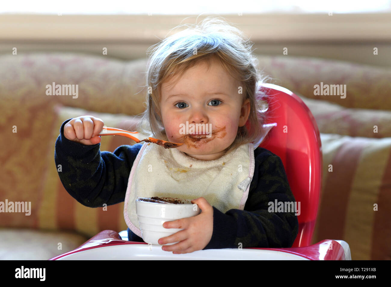 Alimentation bébé fille elle-même avec le chocolat sur son visage Banque D'Images