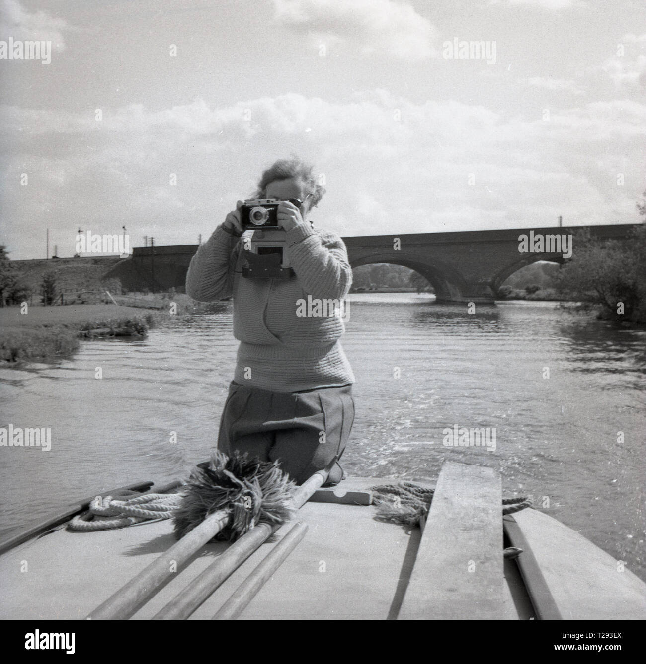 Années 1950, dame agenouillée sur le dos d'un yacht à voile ou bateau à moteur avec un appareil photo prendre une photo, Oxford, Angleterre, Royaume-Uni. Banque D'Images