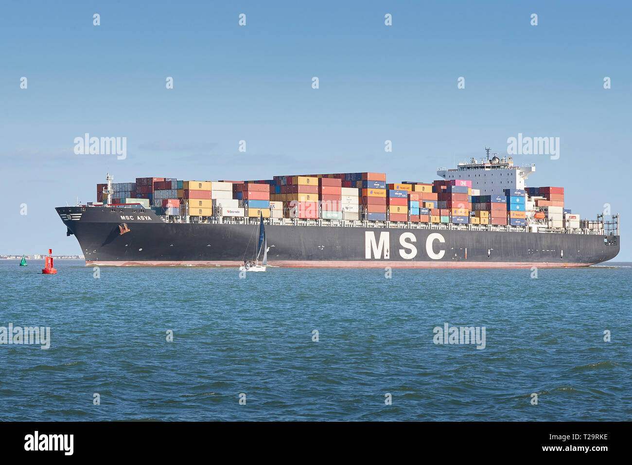 Le porte-conteneurs, MSC ASYA, entre dans le chenal profond comme elle s'approche du port de Southampton, un voilier passant au premier plan, au Royaume-Uni. Banque D'Images