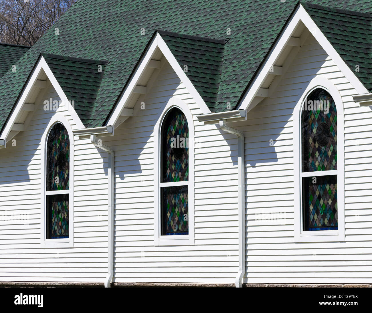 Vue extérieure oblique de toit vert foncé et blanc lumineux mur d'église, avec trois pignons de toit triangulaire au-dessus de trois vitraux Banque D'Images