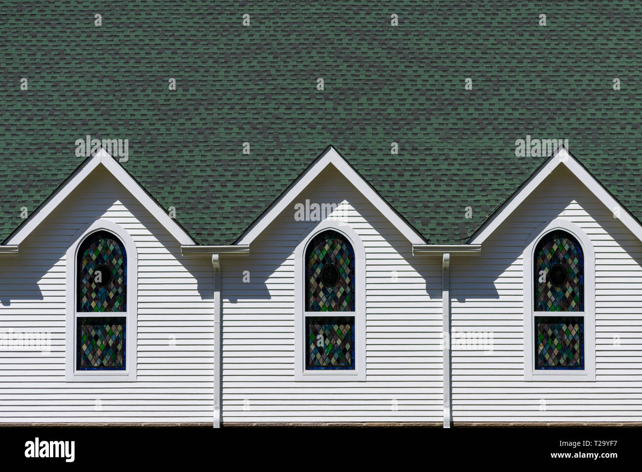 Vue extérieure du toit vert foncé et blanc lumineux mur d'église, avec trois pignons de toit triangulaire au-dessus de trois vitraux Banque D'Images