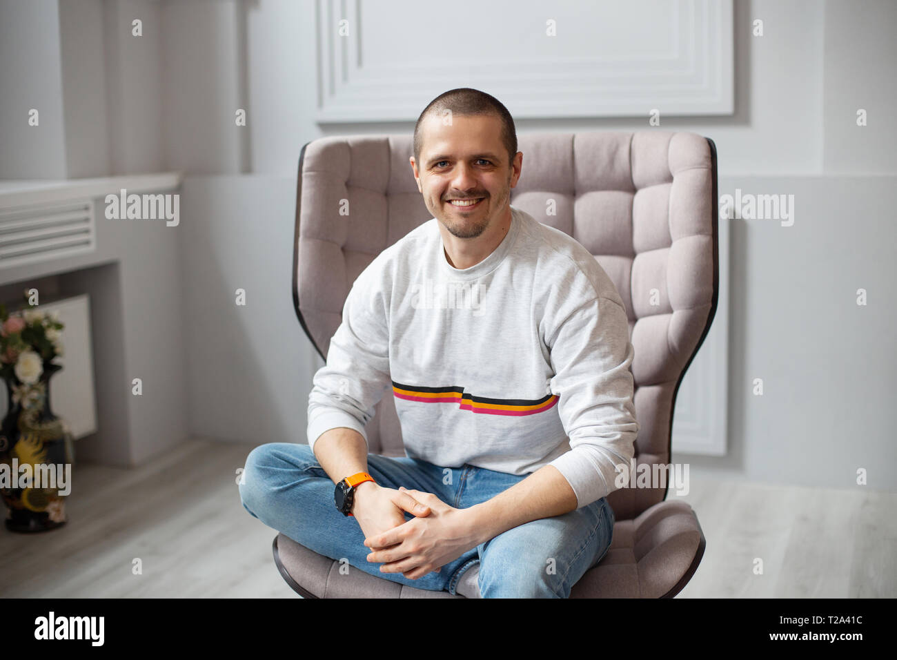 L'homme assis sur une chaise et souriant lookin à huis clos. Portée en jeans Banque D'Images