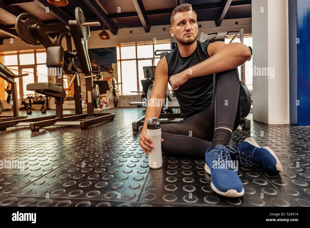 Remise en forme de l'athlète masculin est assis avec un verre dans une salle de sport moderne Banque D'Images