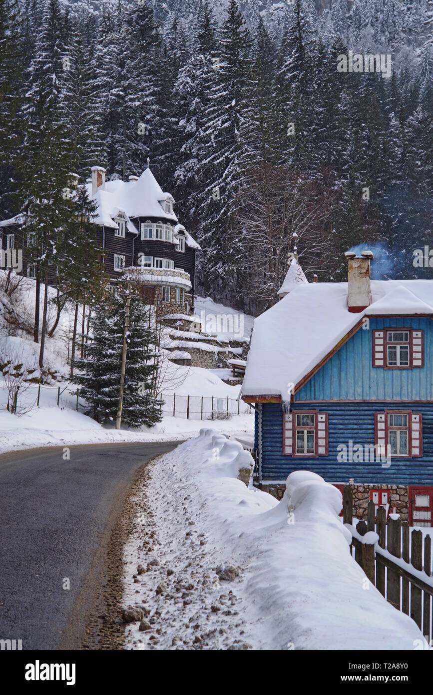 Scène d'hiver dans la région de Red Lake Resort (Roumanie), les maisons couvertes de neige et de forêt près de la route. Banque D'Images