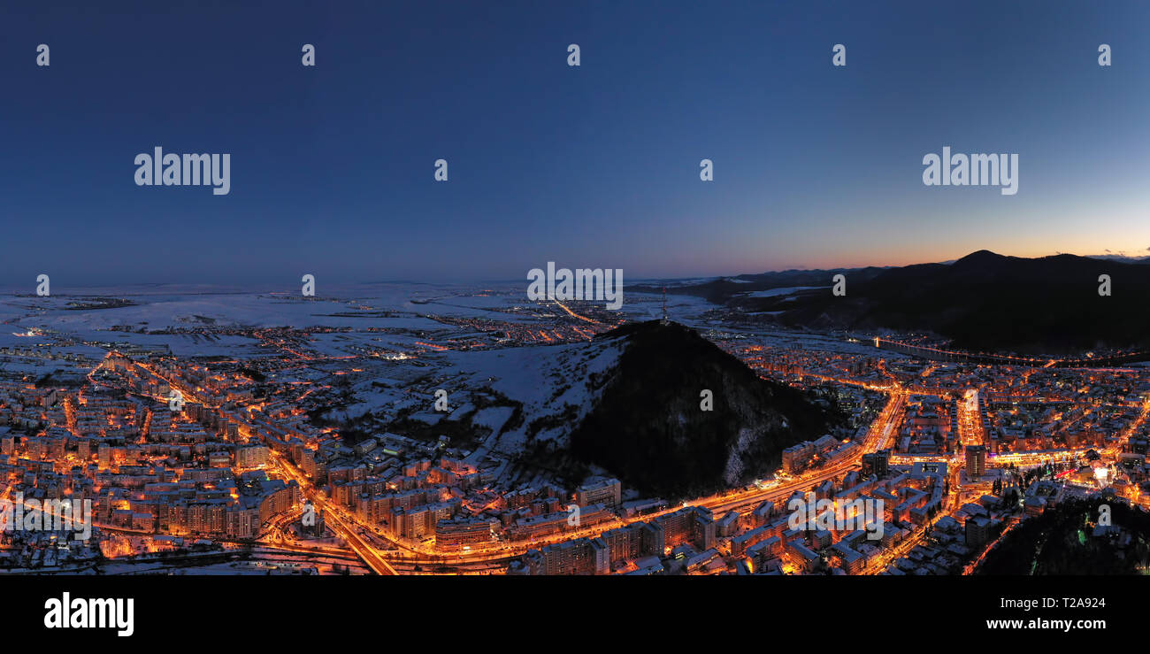 Vue de nuit de drones les lumières et les montagnes derrière, paysage aérien de Brasov en Roumanie, scène d'hiver. Banque D'Images