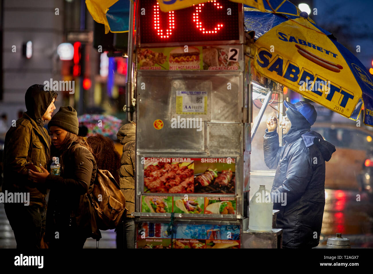 Rue de hot-dog vente de trader à partir de son panier sur la 8e avenue dans le noir soir, Manhattan, New York, USA Banque D'Images